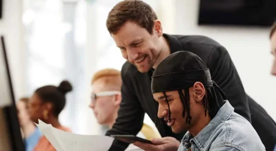 Seitenansicht eines männlichen Lehrers, der einem afroamerikanischen Studenten bei der Computerbenutzung in einem Hörsaal hilft (Freiraum für Text)