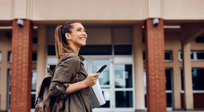 Happy female student texting on smart phone while going to lecture at the university. Copy space.