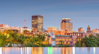 Manchester, New Hampshire, USA Skyline am Merrimack River in der Abenddämmerung.