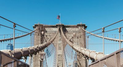 ponte de brooklyn com bandeira americana num fundo de céu azul claro, nova york, eua