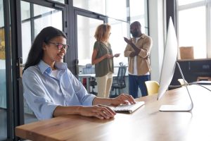 Donna che lavora al computer in un ufficio accogliente. Bella lavoratrice che guarda lo schermo con allegria e sorriso affascinante