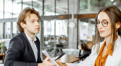 Young man and woman having business conversation while sitting together in the bar or coworking space