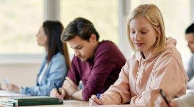 Young female student writing while having lecture at college classroom.