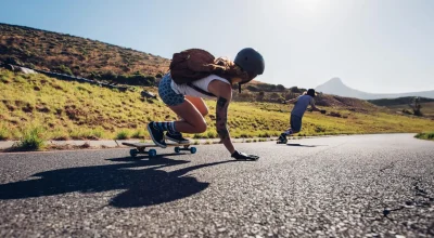 Młodzi przyjaciele jeżdżą na deskorolkach po wiejskiej drodze. Młodzi ludzie jeżdżą na longboardach w słoneczny dzień.