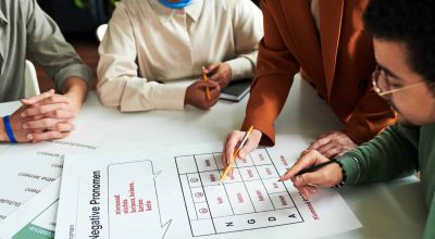 Group of students gathered by table at lesson of German grammar while mature teacher of foreign languages explaining negative pronouns