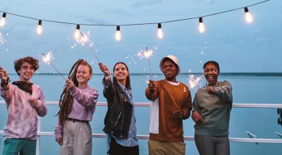 Jeunes gens multiraciaux heureux avec des feux de Bengale étincelants profitant d'une fête en plein air sur une jetée.