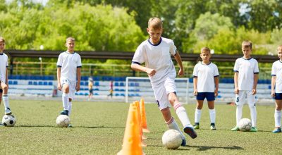 Ritratto di un adolescente che conduce la palla tra i coni durante un allenamento di calcio in un campo in una giornata di sole