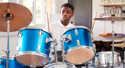 Aluno adolescente do sexo masculino tocando bateria em aula de música