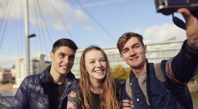 Tre amici seduti all'aperto che scattano selfie con la macchina fotografica, Bristol, Regno Unito